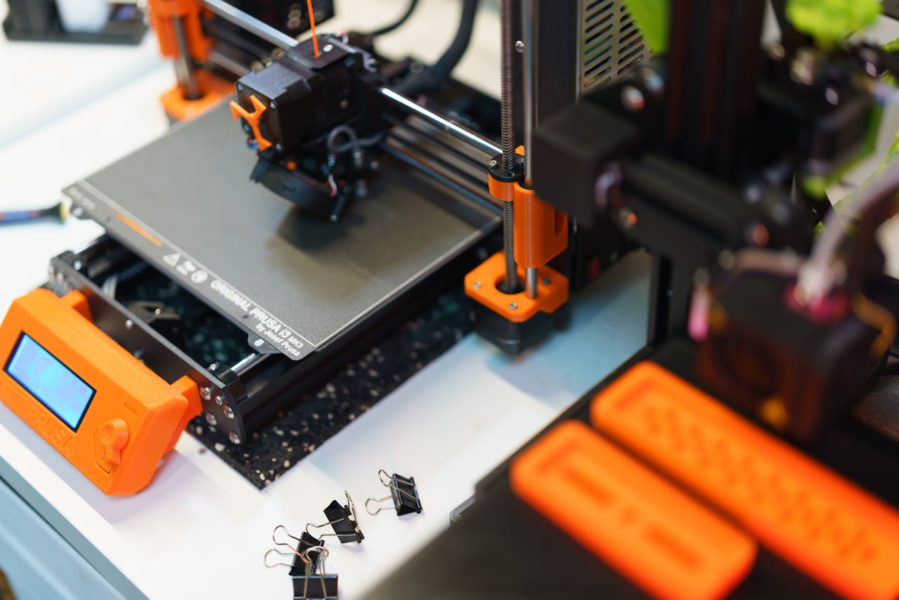 hero-img-01 Detailed view of a 3D printer in a modern industrial setting, showcasing technology and creativity.